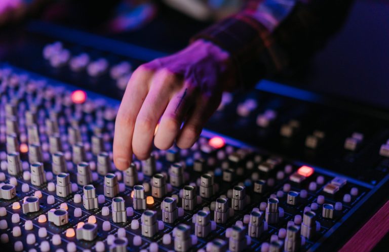 Hand bedient Regler an einem Mischpult mit leuchtenden Tasten.
