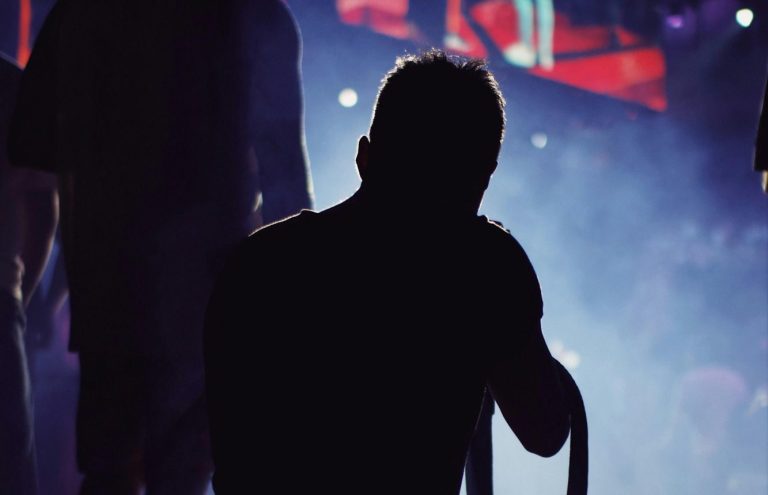 Silhouette einer Person auf einer Bühne mit buntem Licht im Hintergrund.