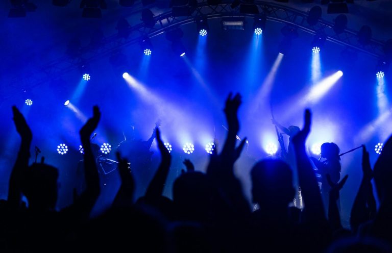 Hände von begeistertem Publikum bei einem Konzert, umgeben von blauen Lichtstrahlen.